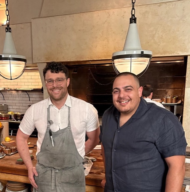 Paul with a chef in front of a wood-fired grill